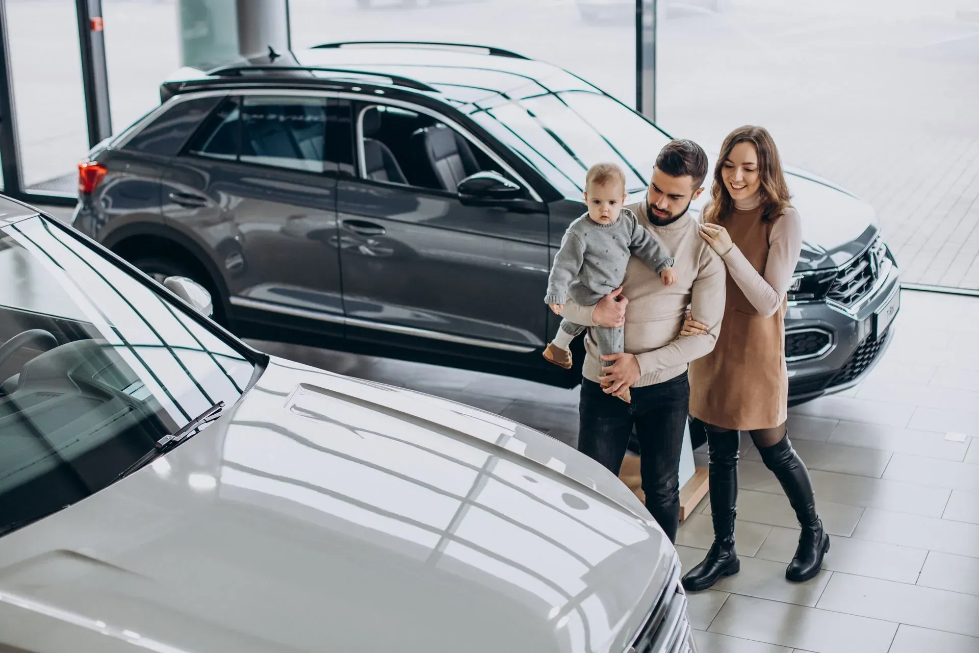 Young family holding a toddler while looking at cars in a dealership showroom